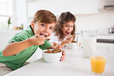 Two children looking at camera while eating cereal