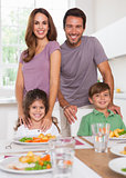Two children and their parents smiling at the camera at dinner table