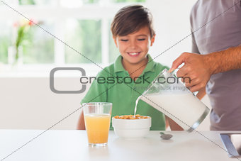 Father putting milk in the cereal of his son
