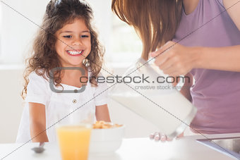Mother putting milk in the cereal of his daughter