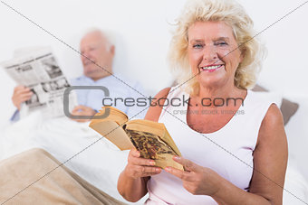 Smiling old couple reading book and newspaper