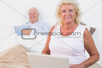 Smiling old couple using a tablet and the laptop