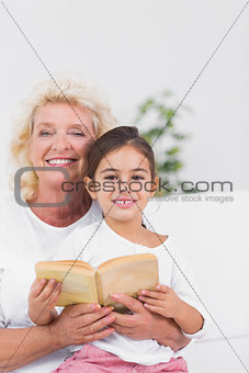 Smiling granddaughter and grandmother reading a novel together