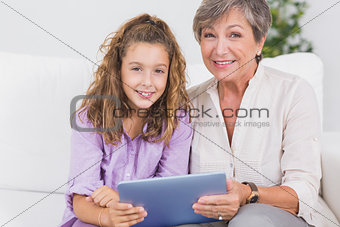 Little girl and her grandmother looking at the camera with tablet pc