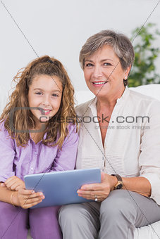 Child and her grandmother looking at the camera with tablet pc