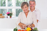Smiling woman cutting vegetables with her husband hugging her from behind