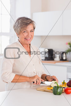 Old woman cutting vegetables on a cutting board with a smile