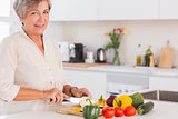 Elderly woman cutting vegetables on a cutting board with a smile