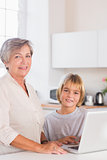 Child and grandmother looking camera with a laptop