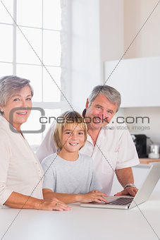 Grandparents and child looking at camera with a laptop