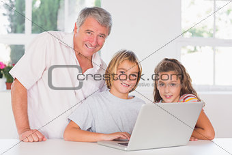Grandfather and children looking at the camera with laptop in front