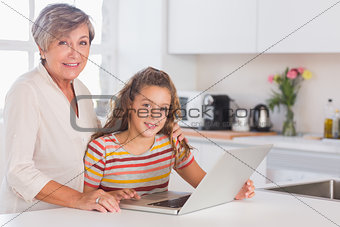 Grandmother and little girl looking at the camera with laptop
