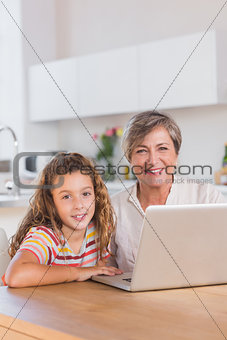 Smiling child and granny looking at the camera with laptop