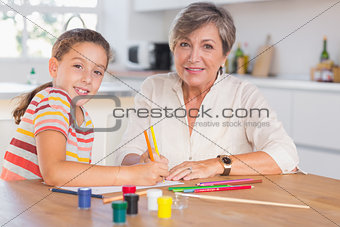 Child with her grandmother looking at the camera while drawing