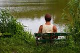 man is sitting on bench on lake