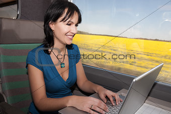 woman in a train computing laptop computer smiling