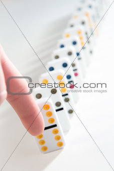 Finger about to knock over line of dominoes