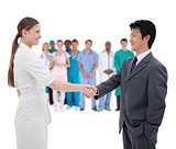Business people shaking hands with medical staff in background
