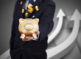 Businessman holding a gold piggy bank with currencies
