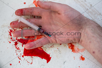 Lifeless hand holding bloody syringe