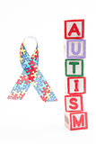 Autism awareness ribbon beside stacked blocks spelling autism