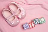 Pink baby slippers and blocks spelling girl