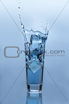 Ice cube falling into glass of water