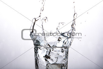 Close up on ice cube falling into glass of water
