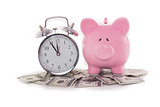 Piggy bank beside alarm clock on dollars