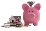 Close up of a pink piggy bank with dollars beside miniature house model