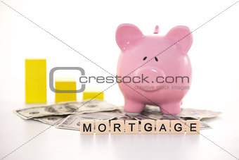 Piggy bank beside graph and mortgage spelled out in plastic letter pieces