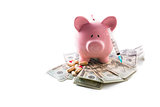 Piggy bank tablets and syringe resting on pile of dollars