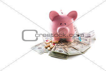 Piggy bank tablets and syringe resting on pile of dollars