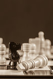 Fallen white chess piece lying next to black knight in sepia tone