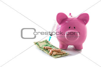 Syringe leaning against piggy bank with dollars and pills