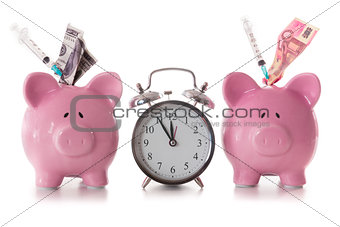 Dollar and euro notes and syringes sticking out of piggy banks with alarm clock