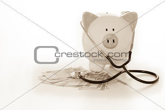 Piggy bank sitting on pile of dollars with stethoscope