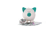 Piggy bank sitting on pile of dollars with mini house