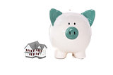 Green and white piggy bank standing beside miniature home