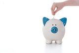 Hand placing coin into blue and white piggy bank