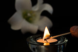 Hand lighting tea light candle with white lily in background