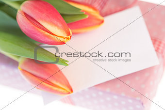 Pink and yellow tulips resting on pink wrapped present with blank card