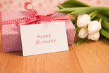 Pink wrapped present with bunch of white tulips and happy birthday card
