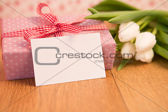 Pink wrapped present with bunch of white tulips and blank card
