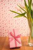 Vase of tulips on wooden table with pink wrapped gift