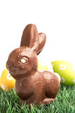 Chocolate bunny rabbit sitting on grass with easter eggs behind