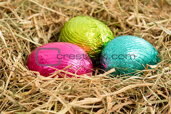Three colouful easter eggs nestled in straw nest