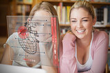 Two smiling students looking at laptop and futuristic interface with heart diagram