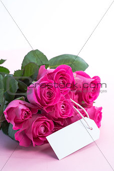 Bouquet of pink roses with an empty card on a table