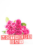 Bouquet of pink roses next to wooden blocks spelling mothers day